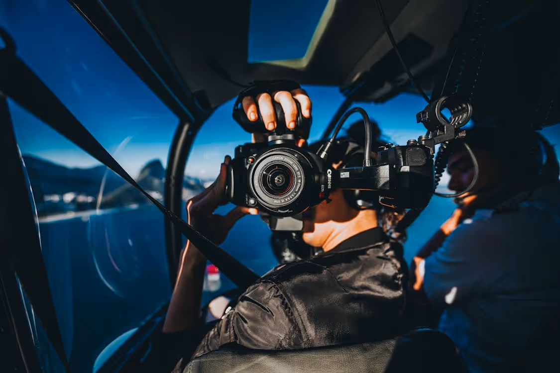 man taking a photo with a professional camera while seated in a helicopter cockpit flying over a body of water