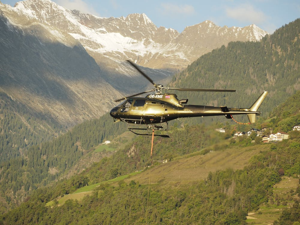 helicopter with sling flying over forest-covered mountains