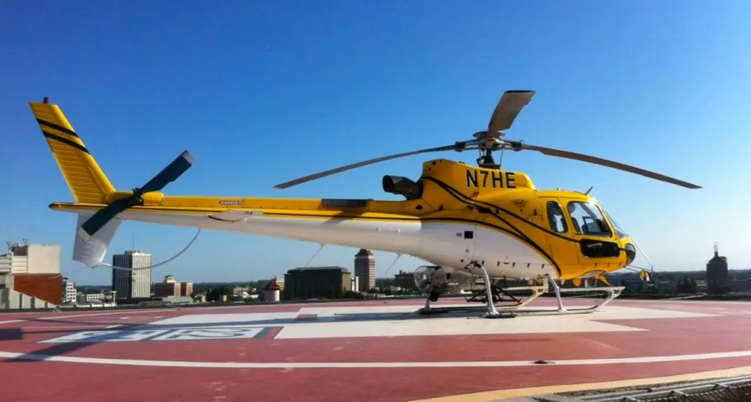 yellow, black, and white Airbus AS-350 B3 helicopter from Helicopter Express resting on a red and white tarmac under blue skies