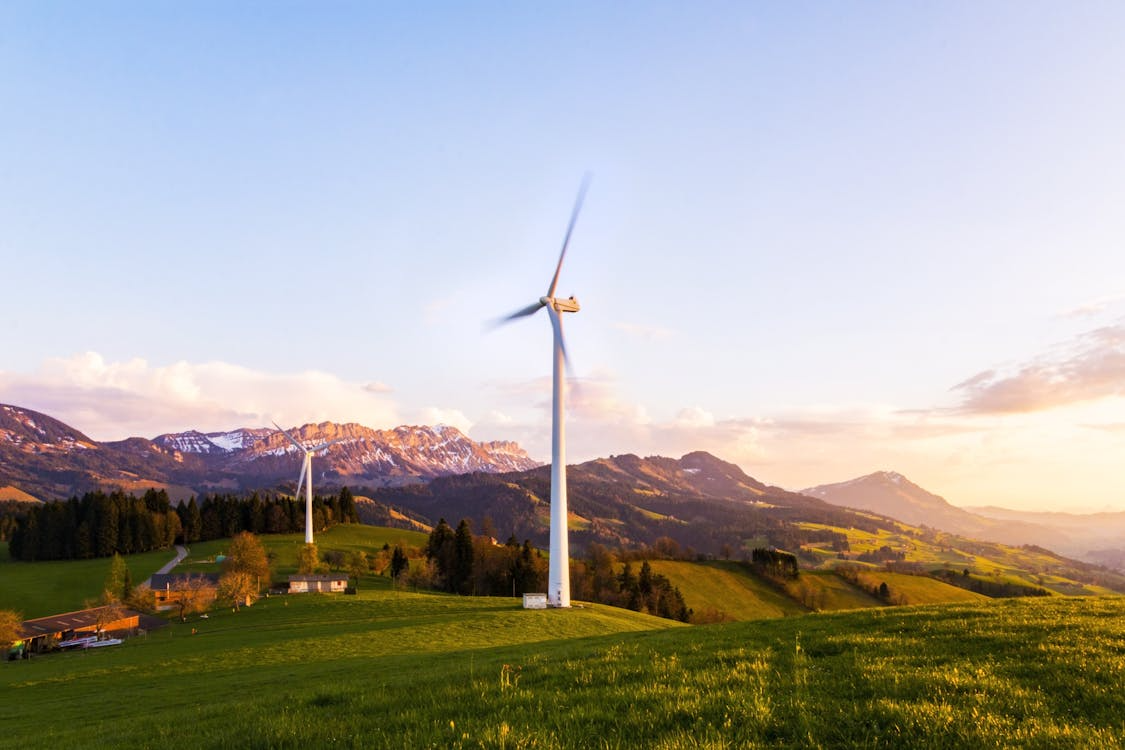 sustainable energy windmill farm on grassy slopes with mountains in the background