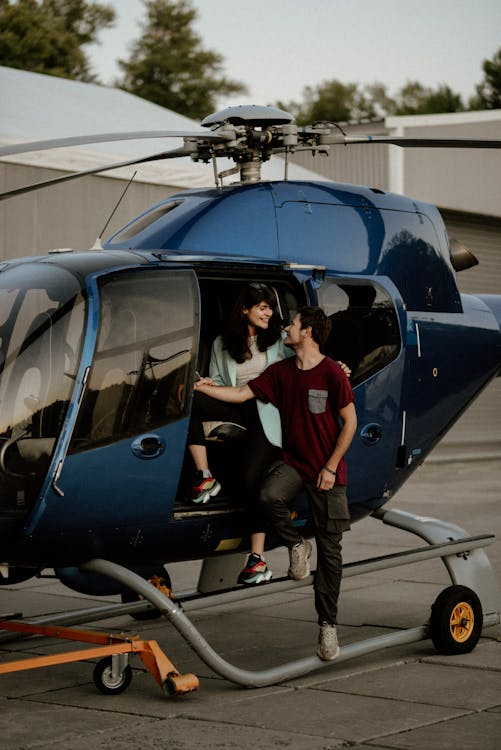 happy young couple looking into each other's eyes as they climb out of a blue helicopter