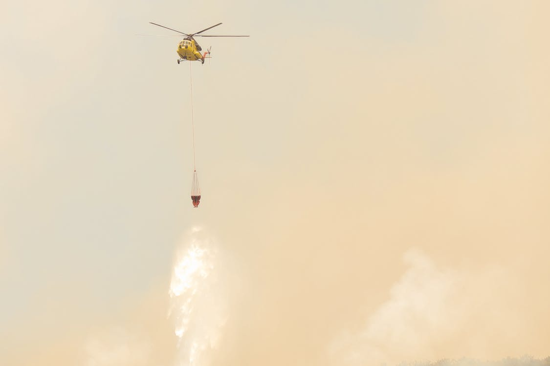yellow aerial firefighting helicopter using a Bambi Bucket to drop water onto a wildfire below