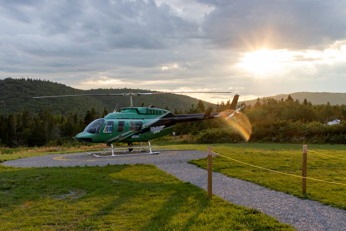 green and black helicopter on a landing pad surrounded by forested mountains at sunset