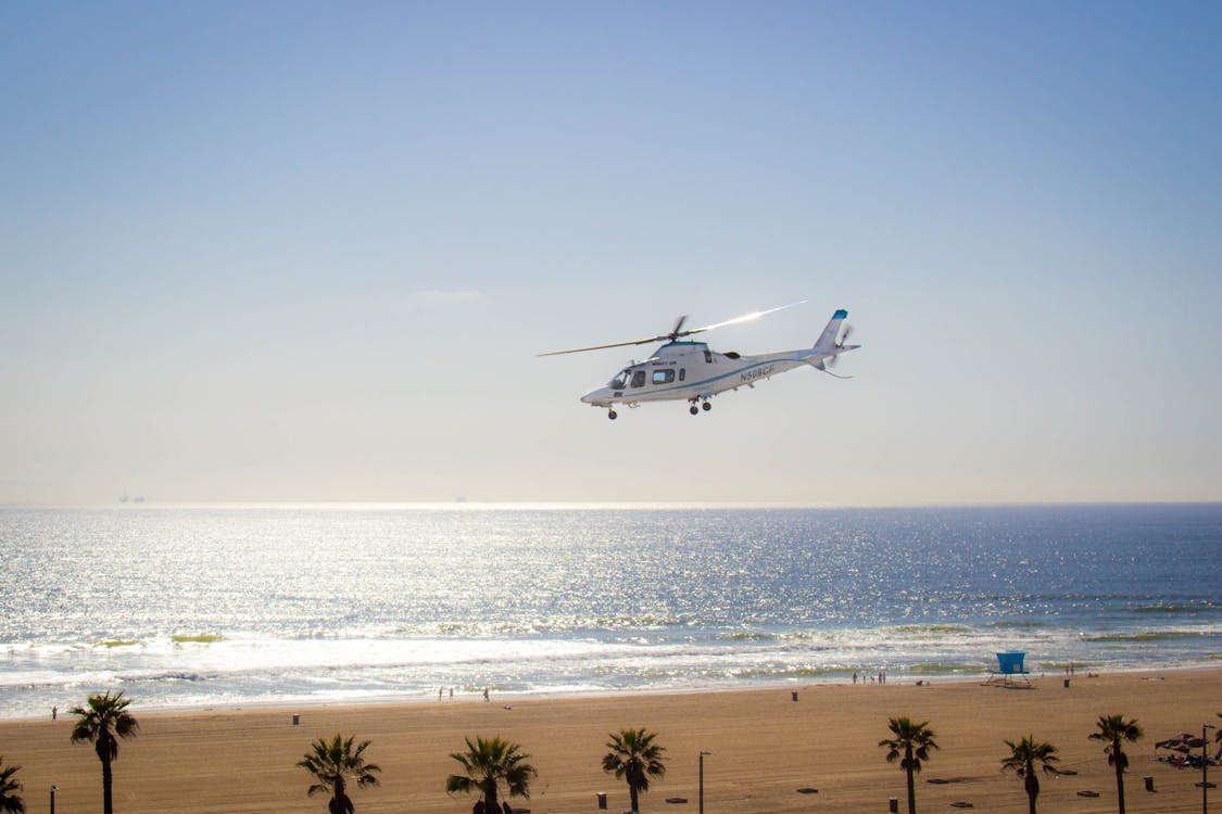 white helicopter flying low over a shoreline on a sunny day at the beach