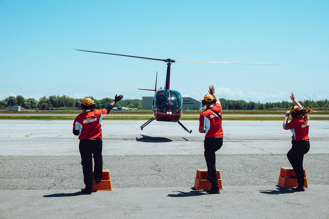 helicopter crew members directing a helicopter as it lands on a concrete surface