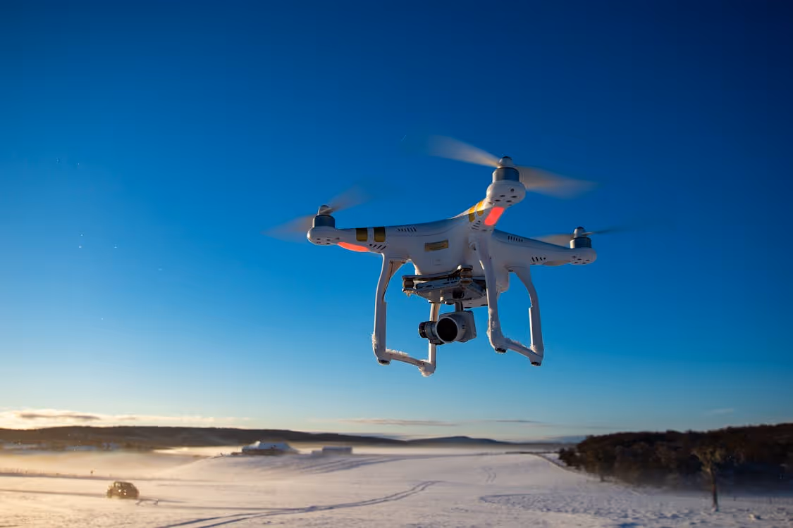 white drone equipped with camera flying over snow-covered fields