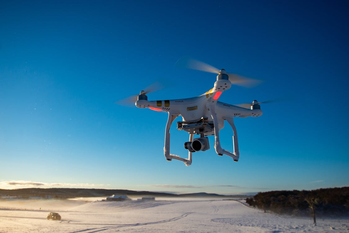 white drone equipped with camera flying over snow-covered fields