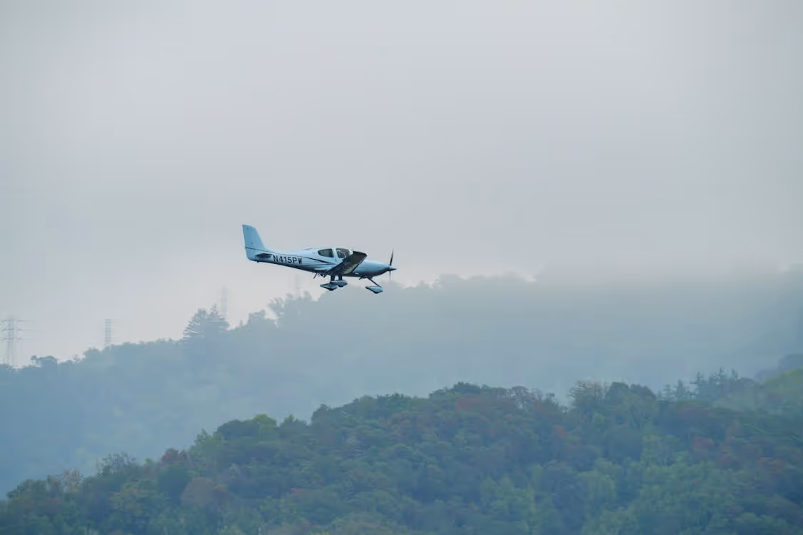 small airplane flying over foggy forested hills