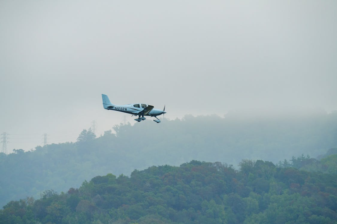 small airplane flying over foggy forested hills