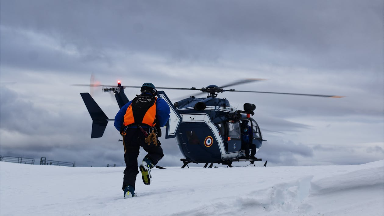 man in reflective vest running toward a helicopter resting on snow-covered ground