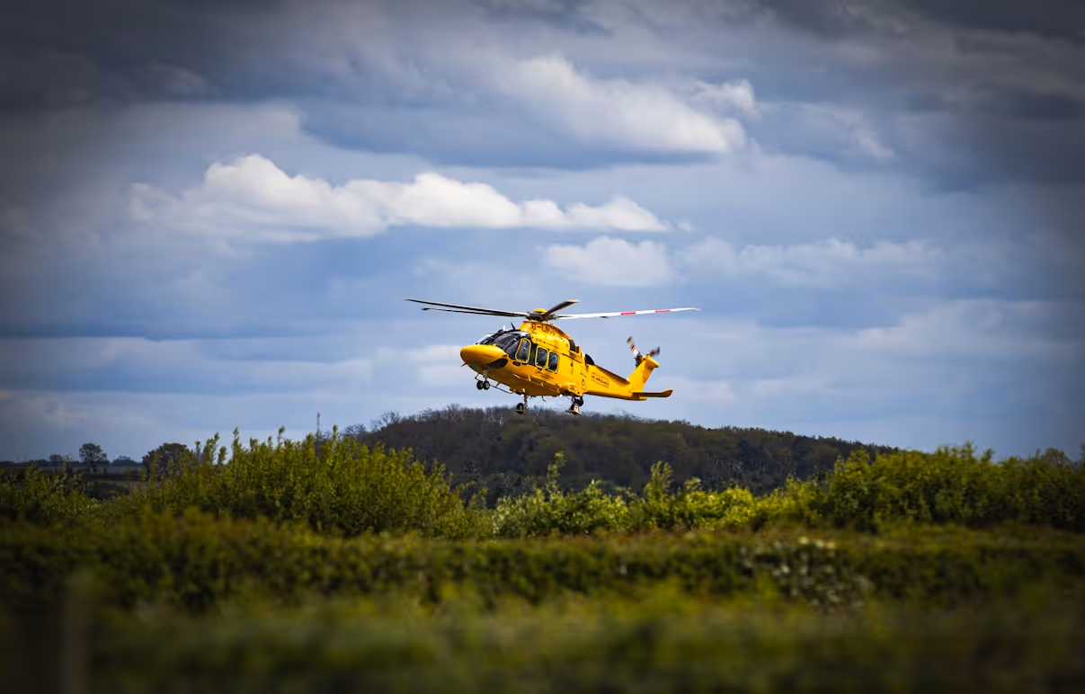 yellow helicopter flying over greenery on a cloudy day