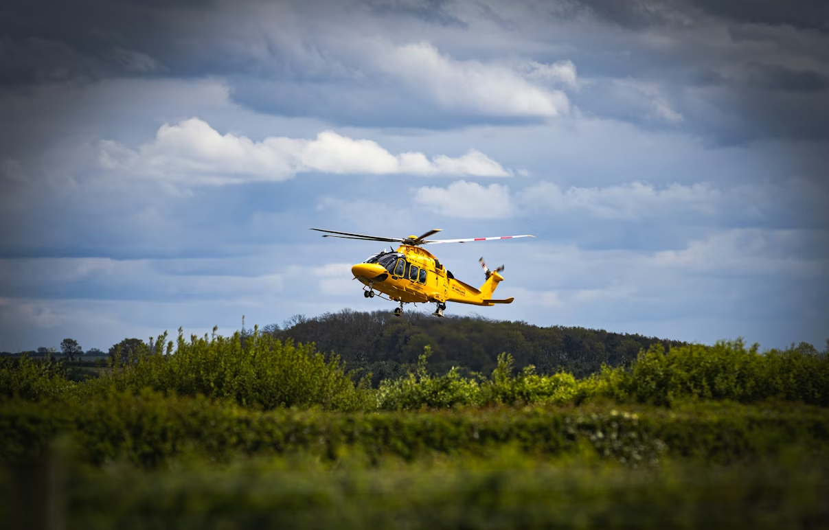 yellow helicopter flying over greenery on a cloudy day