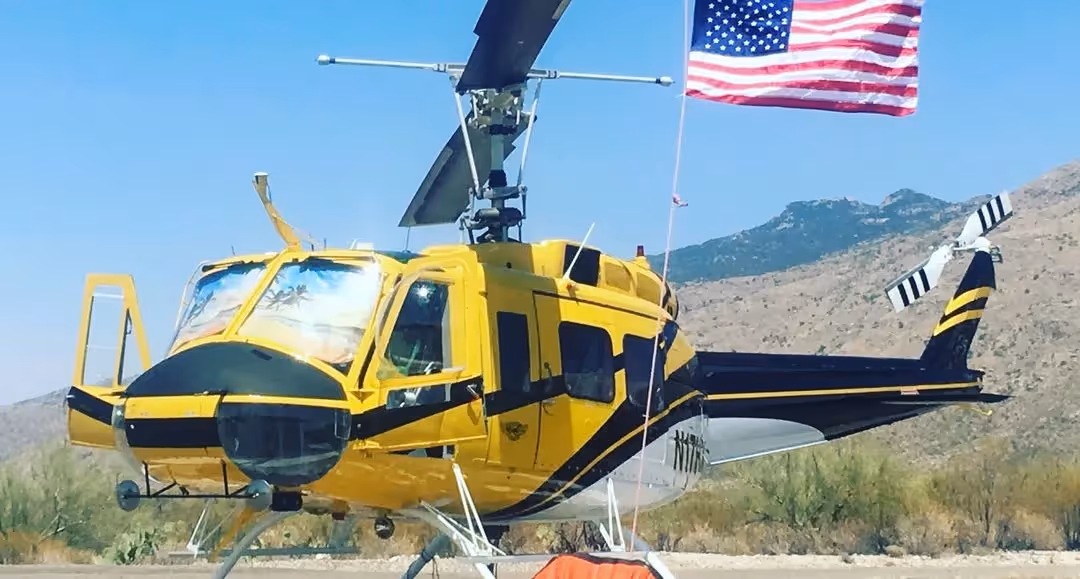 yellow and black Bell 205A-1++ helicopter sitting behind an American flag with mountains in the background