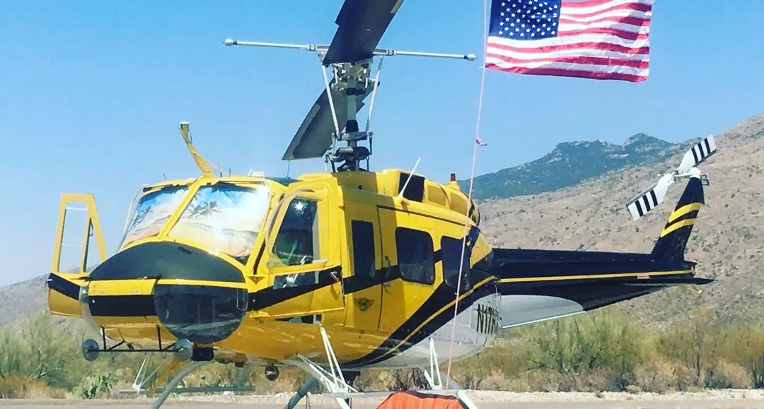 yellow and black Bell 205A-1++ helicopter sitting behind an American flag with mountains in the background
