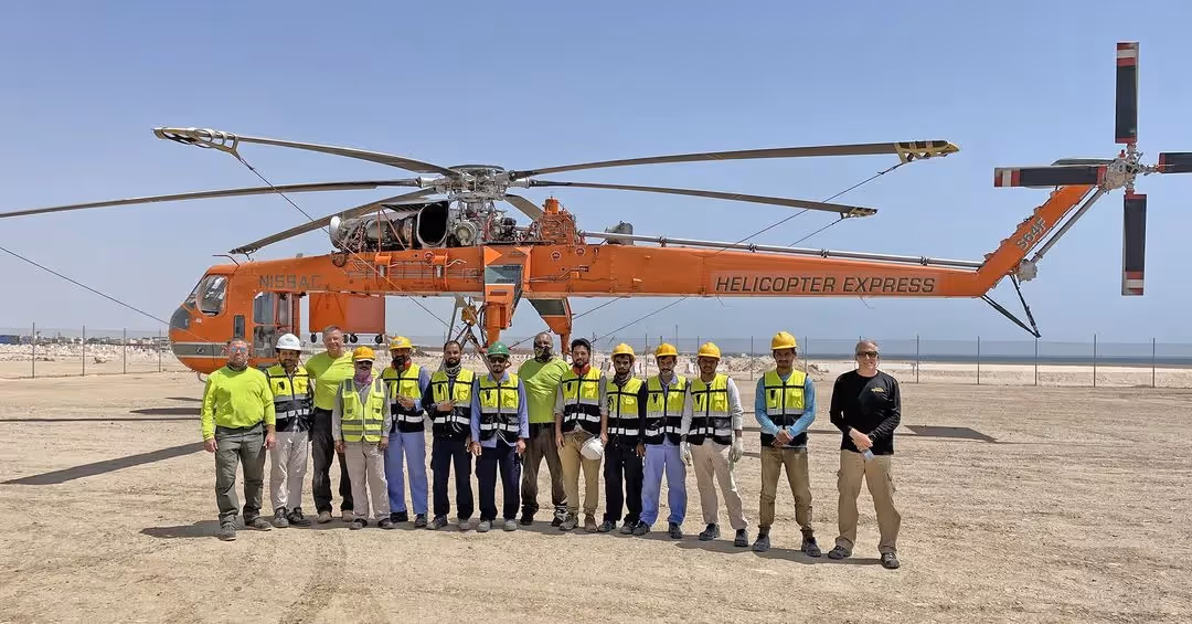 Helicopter Express team standing in front of an orange Sikorsky S-64 Skycrane helicopter on a clear day