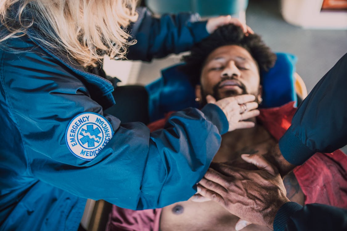 paramedic with blonde hair opening a man's airway while another paramedic does compressions