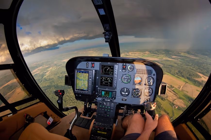 view from inside a helicopter cockpit showing flight controls and gray clouds ahead