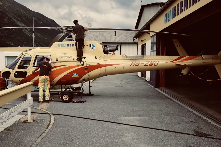 two helicopter maintenance technicians working on a red and yellow helicopter under cloudy skies
