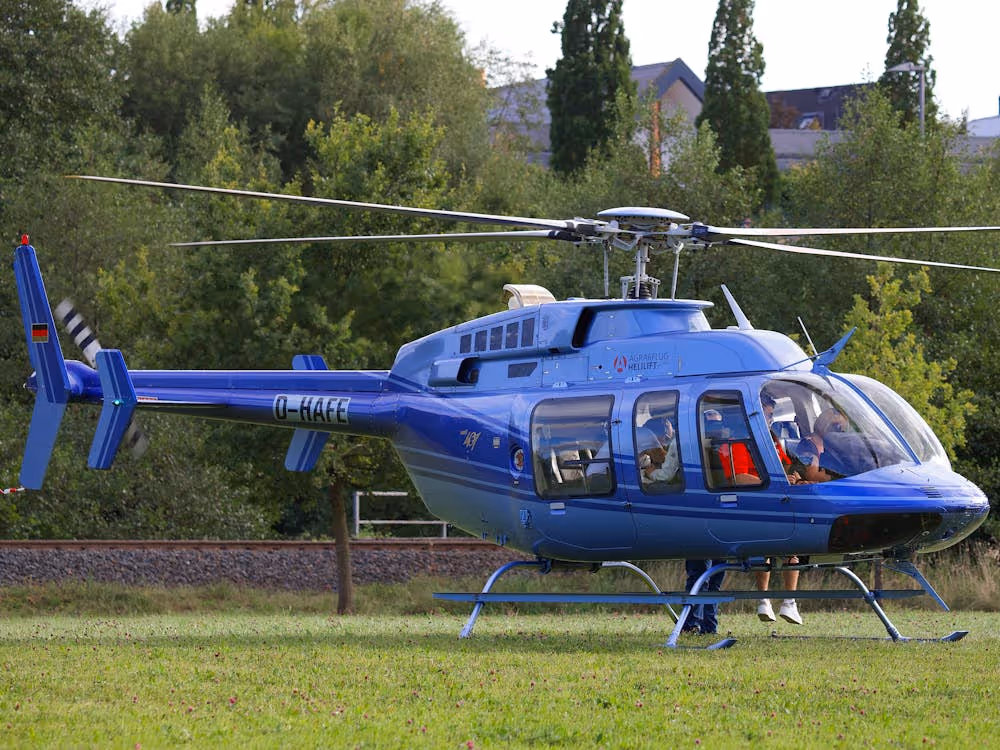 blue helicopter with passengers inside parked on grass in front of trees
