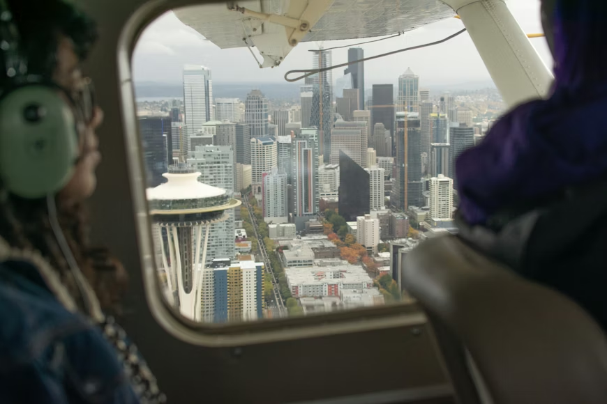 passengers in a helicopter cockpit with high-rise buildings of Seattle out the window
