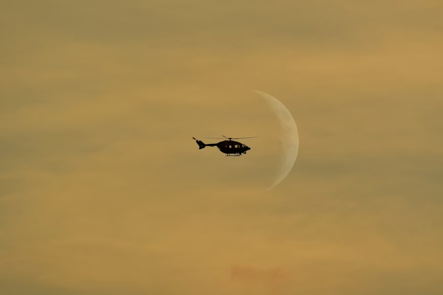 silhouette of a helicopter flying in front of the moon at dusk