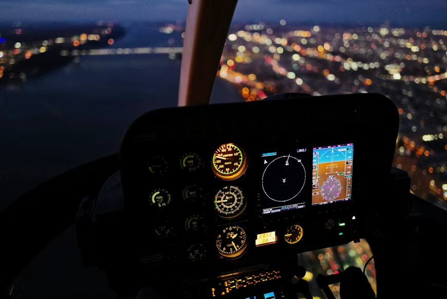 aerial night view of aircraft controls and a brightly lit city from inside a helicopter cockpit