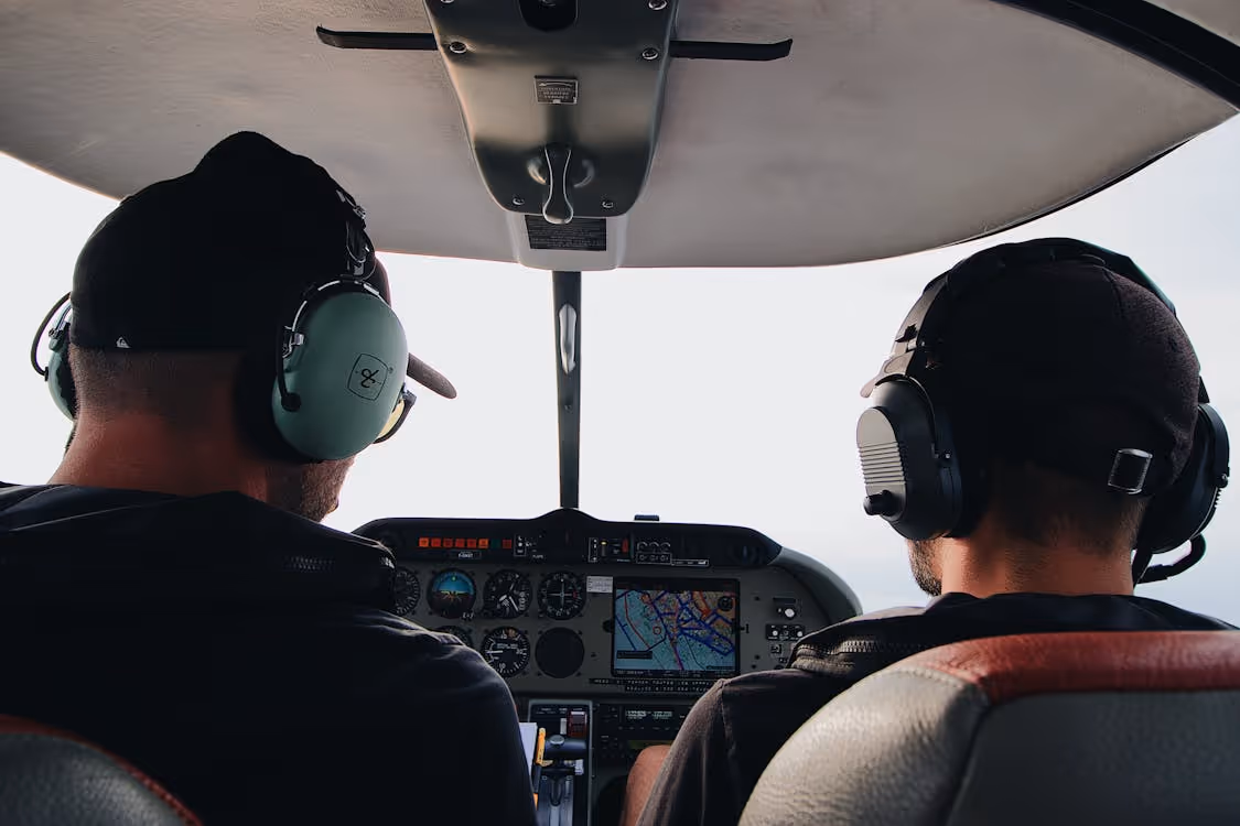 two male helicopter pilots wearing headsets sitting in a cockpit during flight