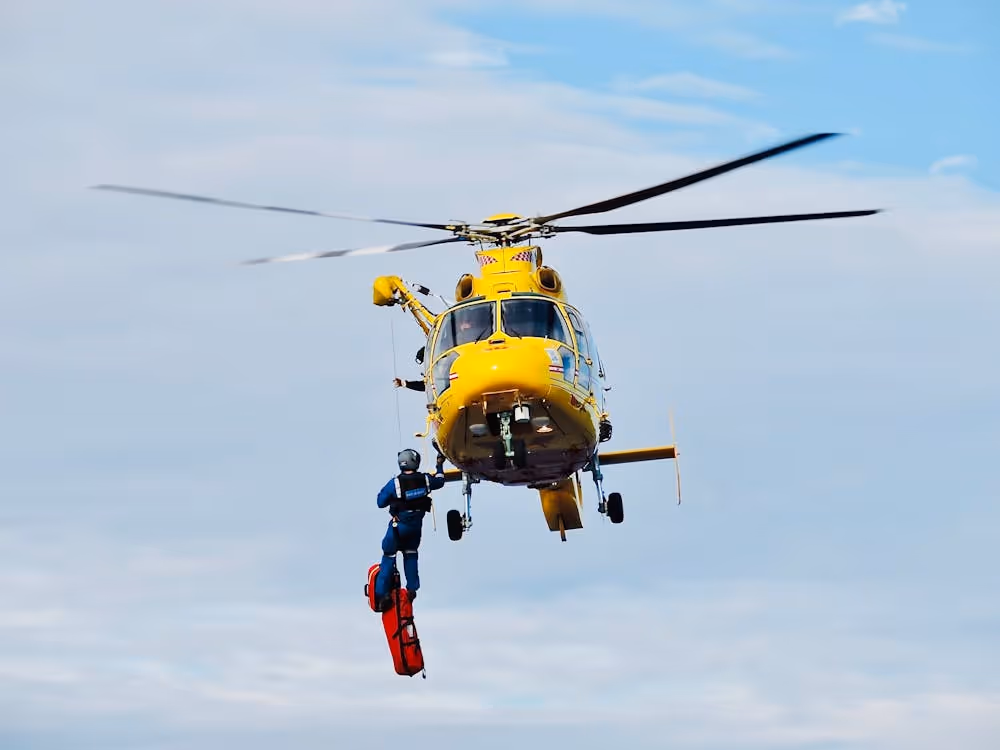 emergency response worker rappelling from a yellow helicopter on a long line to deliver supplies