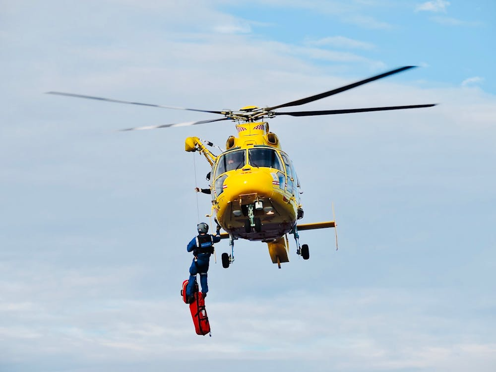 emergency response worker rappelling from a yellow helicopter on a long line to deliver supplies
