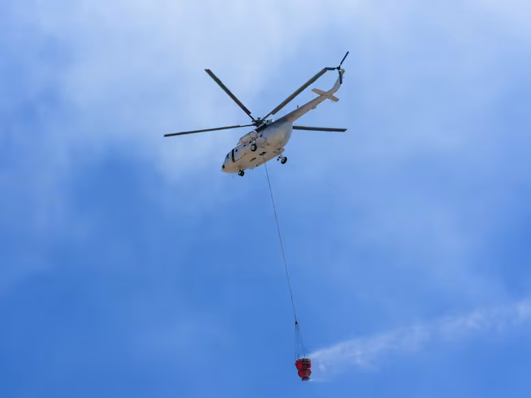 white aerial firefighting helicopter carrying a Bambi Bucket under blue skies