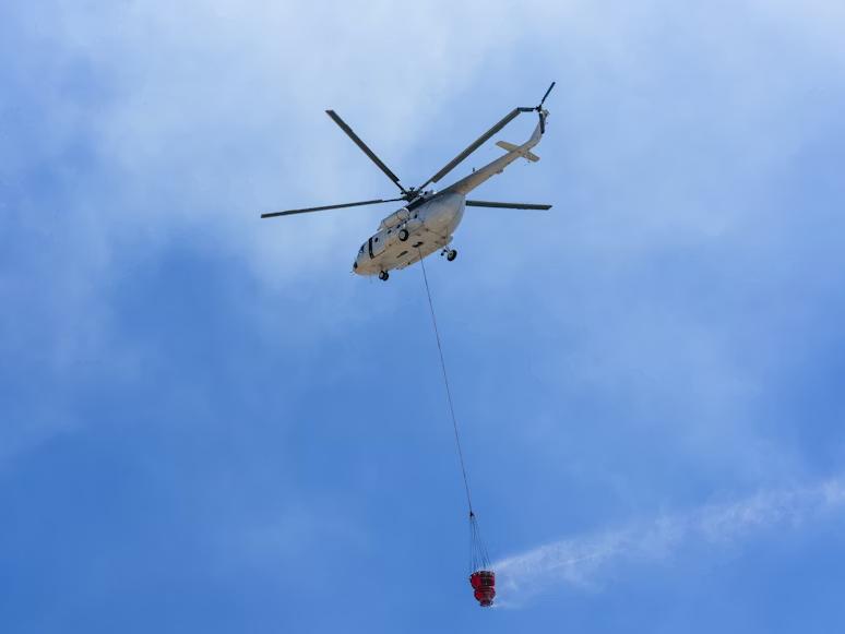 white aerial firefighting helicopter carrying a Bambi Bucket under blue skies