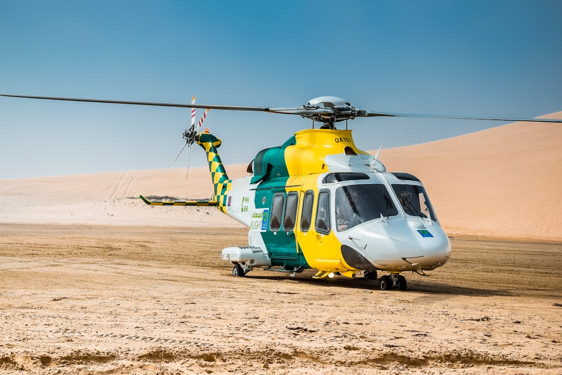 green, yellow, and white medical helicopter resting on desert sand in Qatar