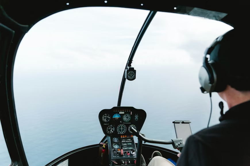 helicopter pilot in the cockpit wearing a headset while flying over the ocean