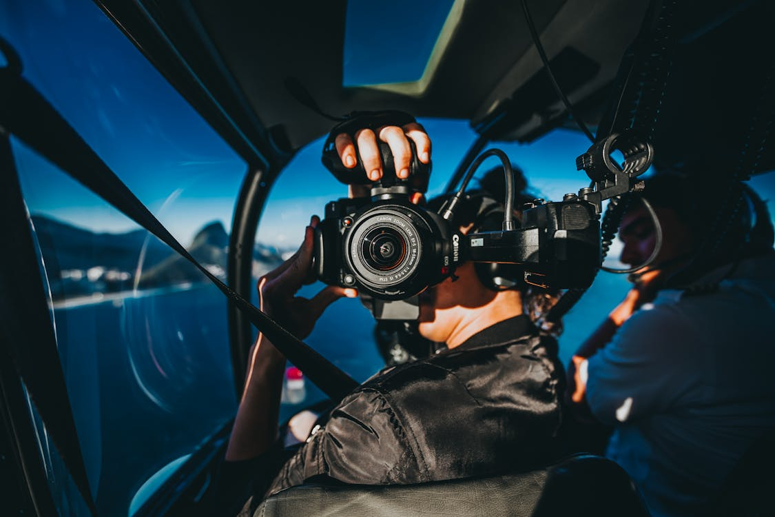 man in a helicopter cockpit taking pictures while flying over a body of water