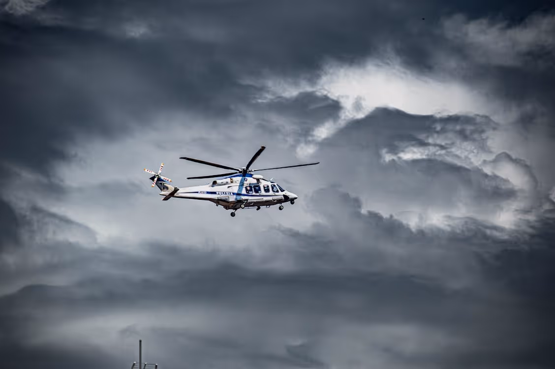 white helicopter flying toward turbulent dark clouds