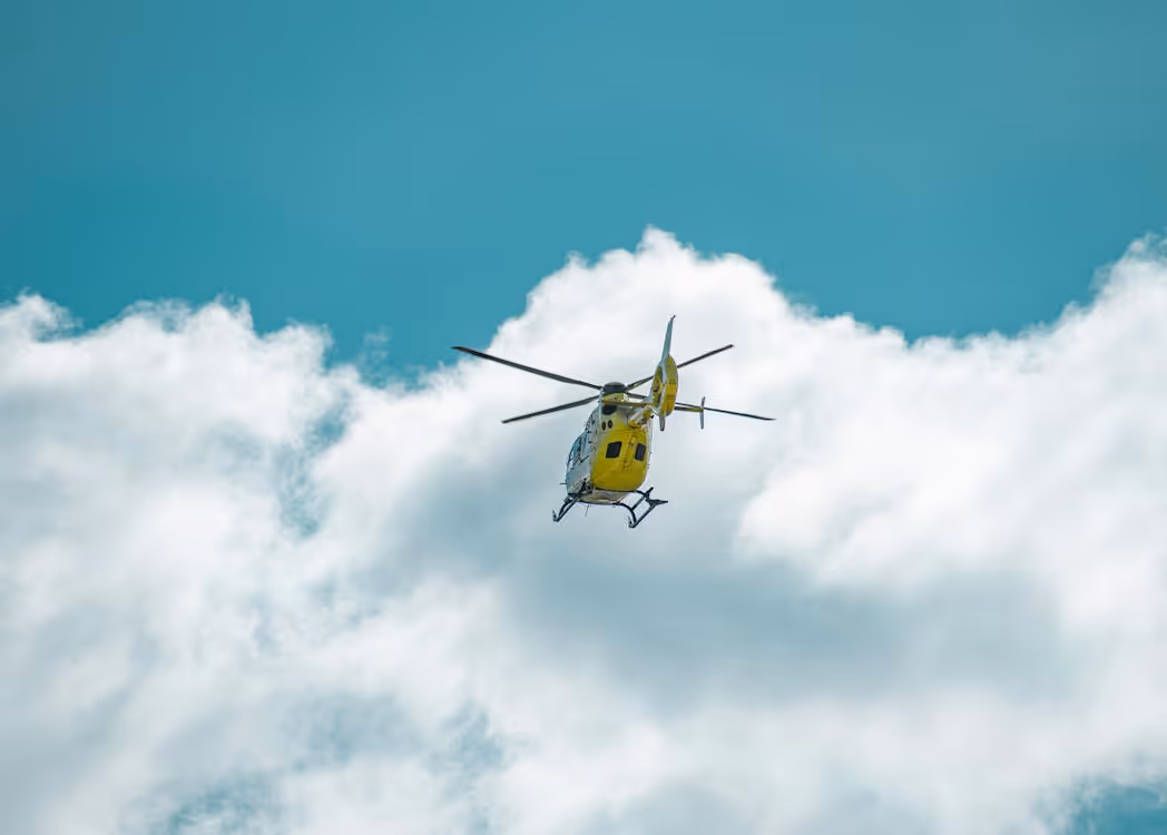 yellow and white helicopter flying toward white clouds on a blue sky day