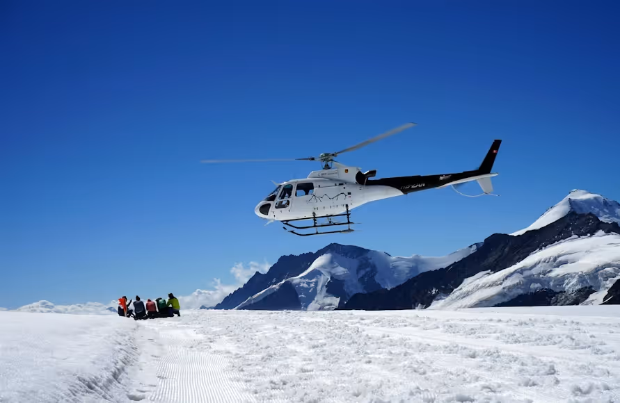 white and black helicopter landing on a flat, snowy surface beside a group of people