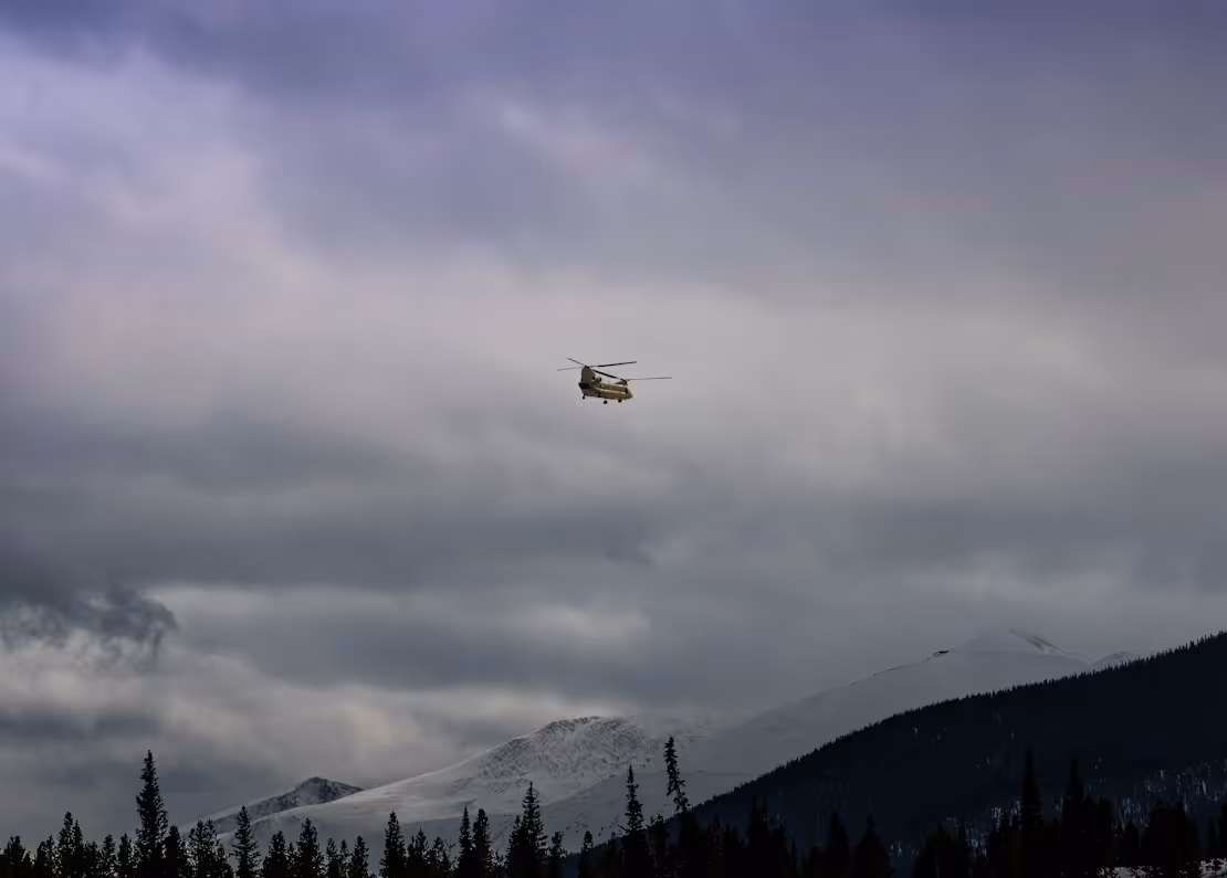 yellow helicopter flying over snow-covered mountains in cloudy skies