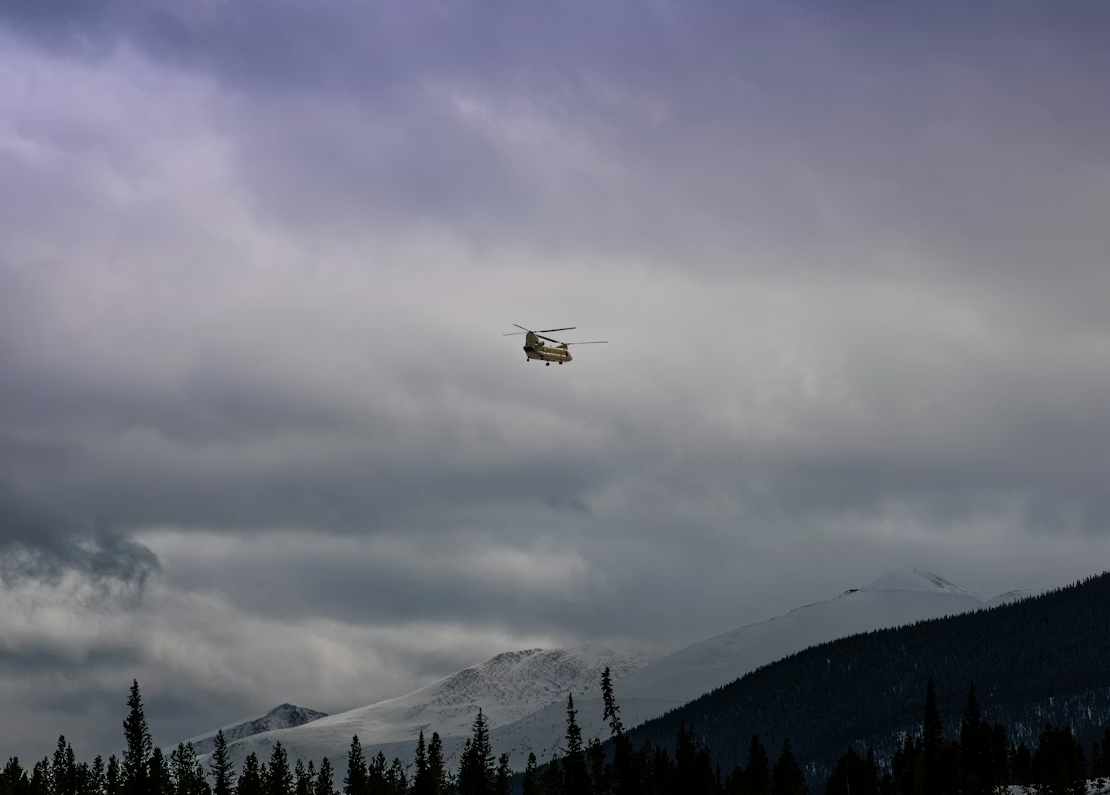 yellow helicopter flying over snow-covered mountains in cloudy skies