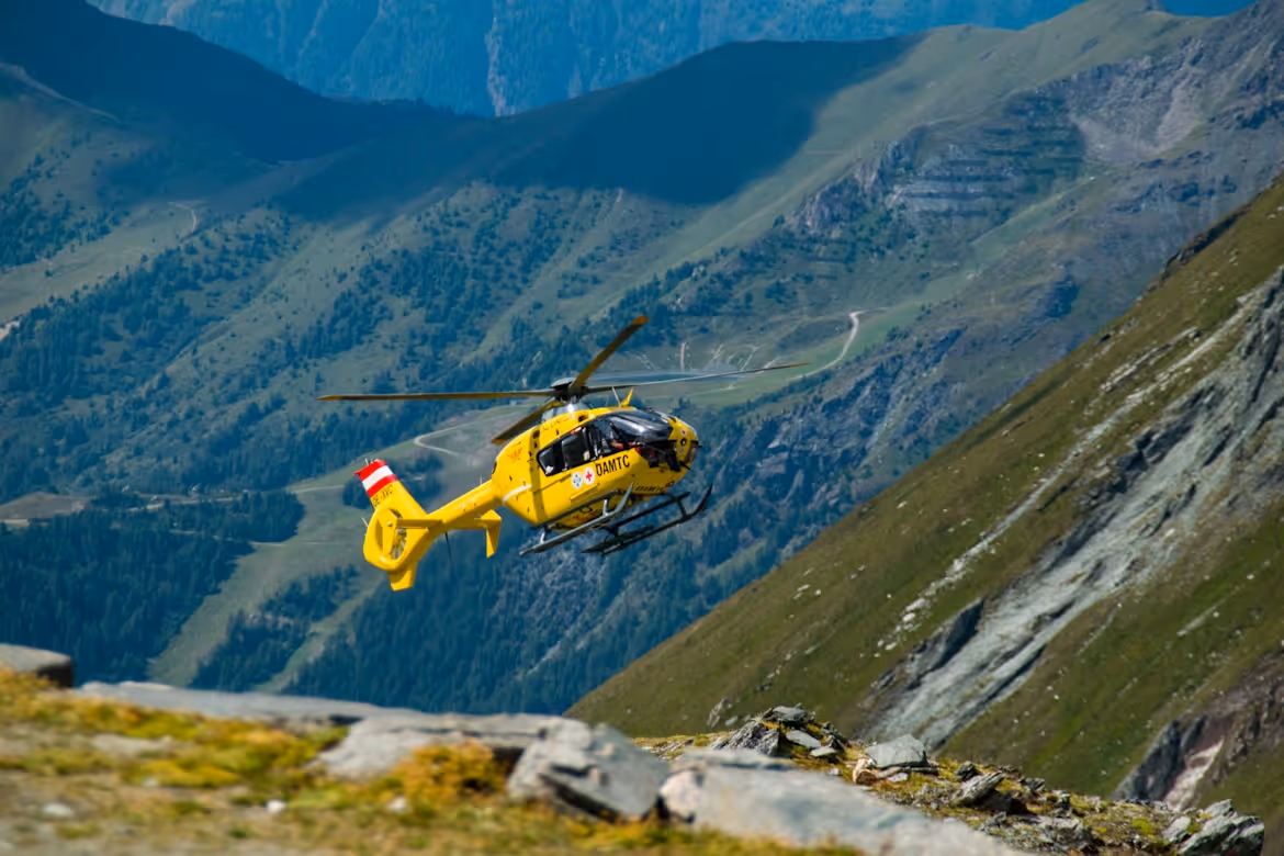 yellow helicopter flying low and close to a grass-covered mountain