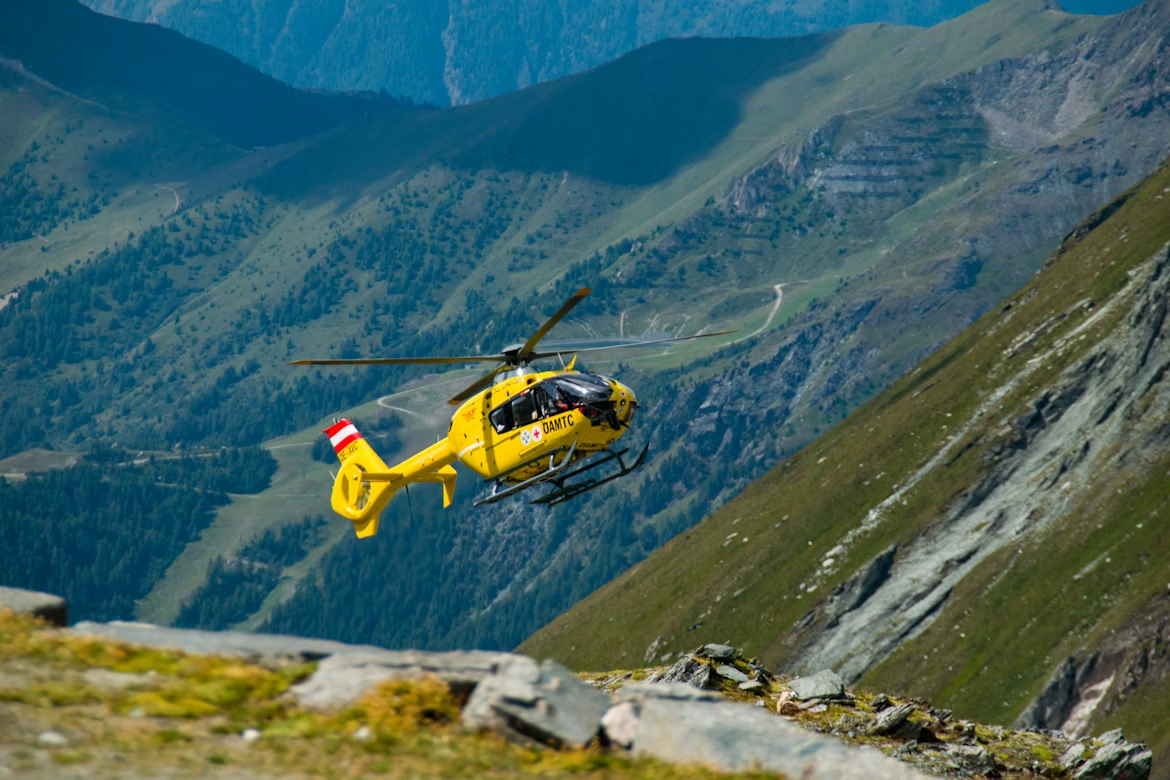 yellow helicopter flying low and close to a grass-covered mountain