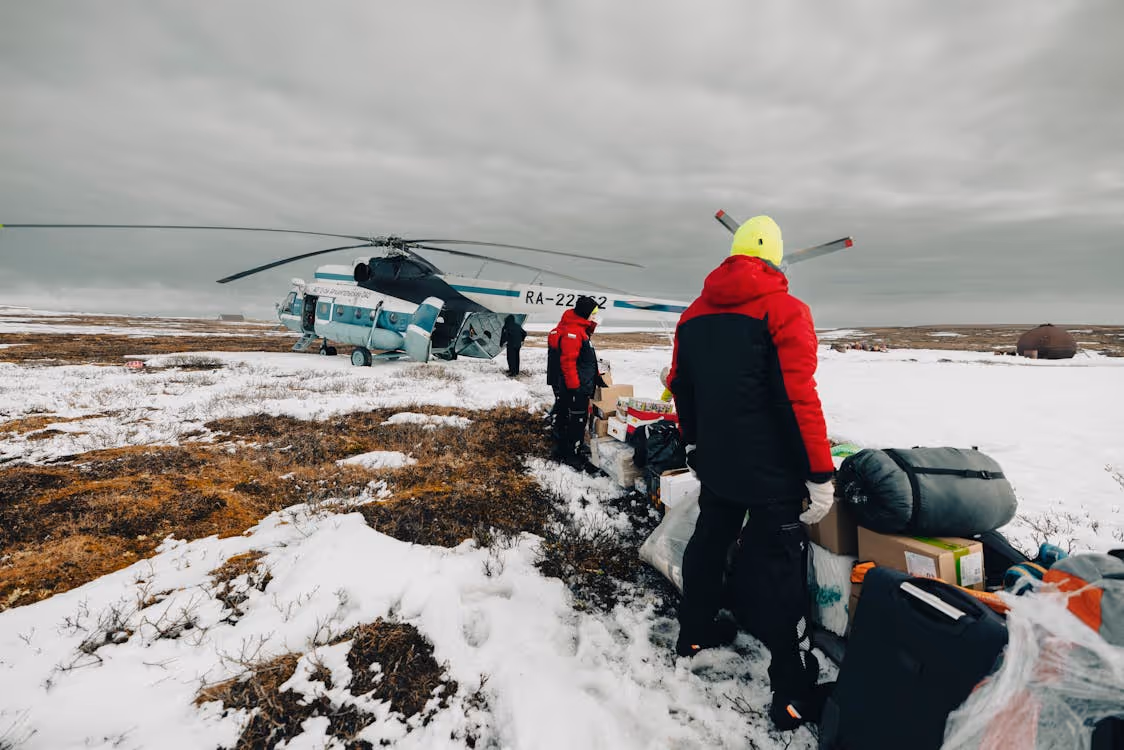 men with supplies beside a white helicopter during a supply drop in the Arctic tundra
