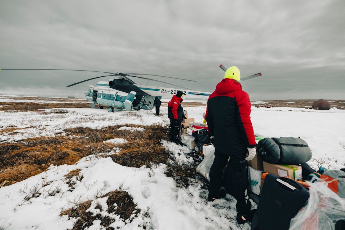men with supplies beside a white helicopter during a supply drop in the Arctic tundra