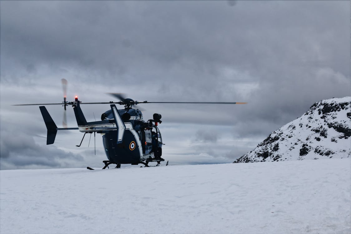 navy and white helicopter resting on snow-covered ground under cloudy skies