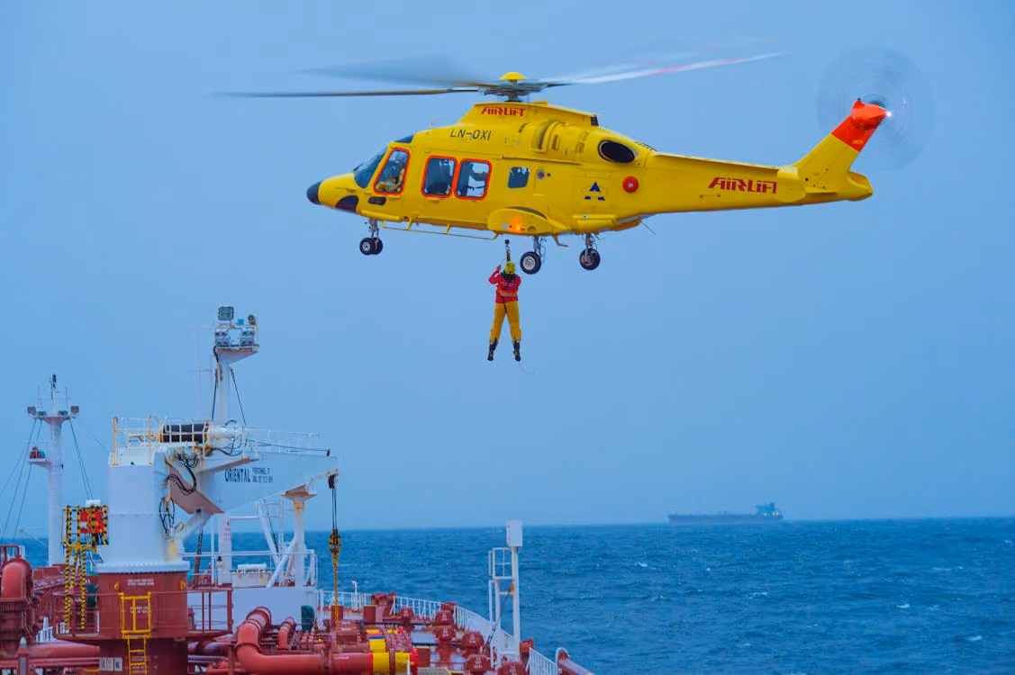 yellow rescue helicopter hovers above a ship while a hoist lifts a person from the ship deck