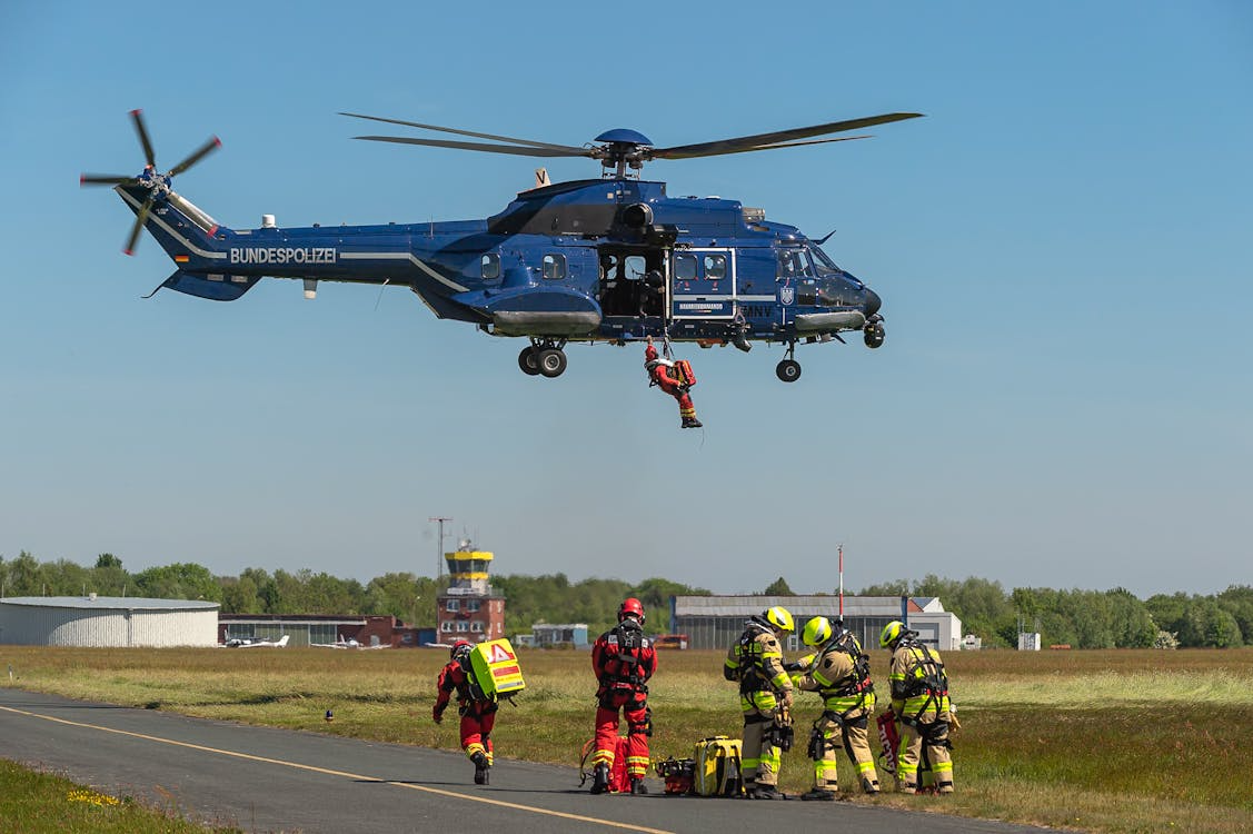 German police helicopter conducting hoist training with rescue personnel in an outdoor field under blue skies