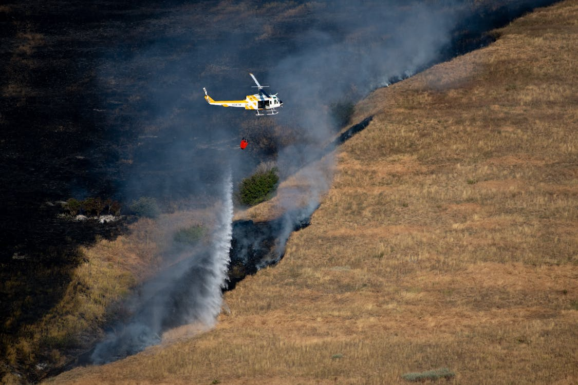 yellow and white helicopter using a Bambi Bucket to extinguish a wildfire in a dry field in Montana