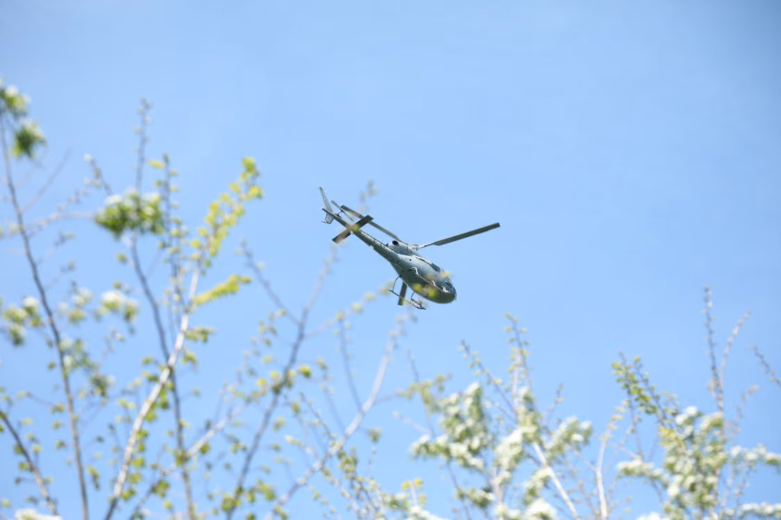 green helicopter flying through clear blue skies over spring foliage