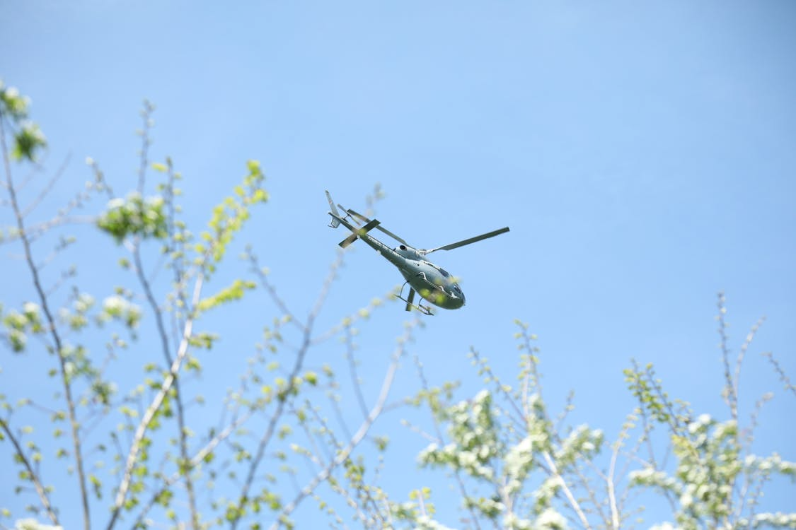 green helicopter flying through clear blue skies over spring foliage