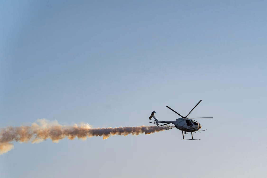 helicopter flying through blue skies while spraying an agricultural treatment